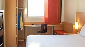 A hotel room with a bed, a desk, a chair, a TV, and a wardrobe.