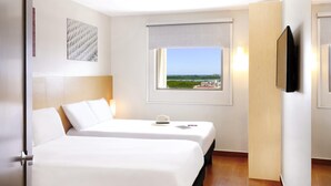 Quarto de hotel com duas camas, janela com vista, televisão na parede e um quadro decorativo.