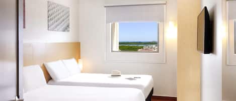 Habitación de hotel con dos camas, una ventana con vistas, un televisor montado y un cuadro en la pared.