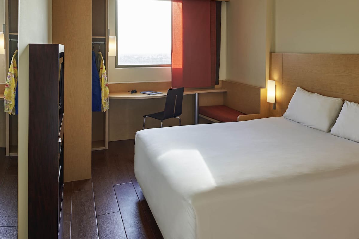 Una habitación de hotel con cama, escritorio, silla, armario y ventana.