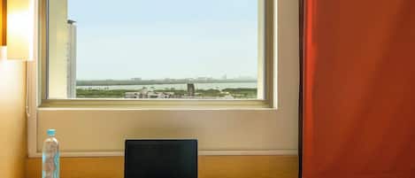 Una computadora portátil sobre un escritorio junto a una ventana con vistas a un paisaje urbano y agua.