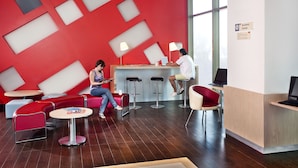 Interior moderno com design geométrico nas paredes em vermelho e branco, várias áreas de estar e um balcão de recepção com um computador.