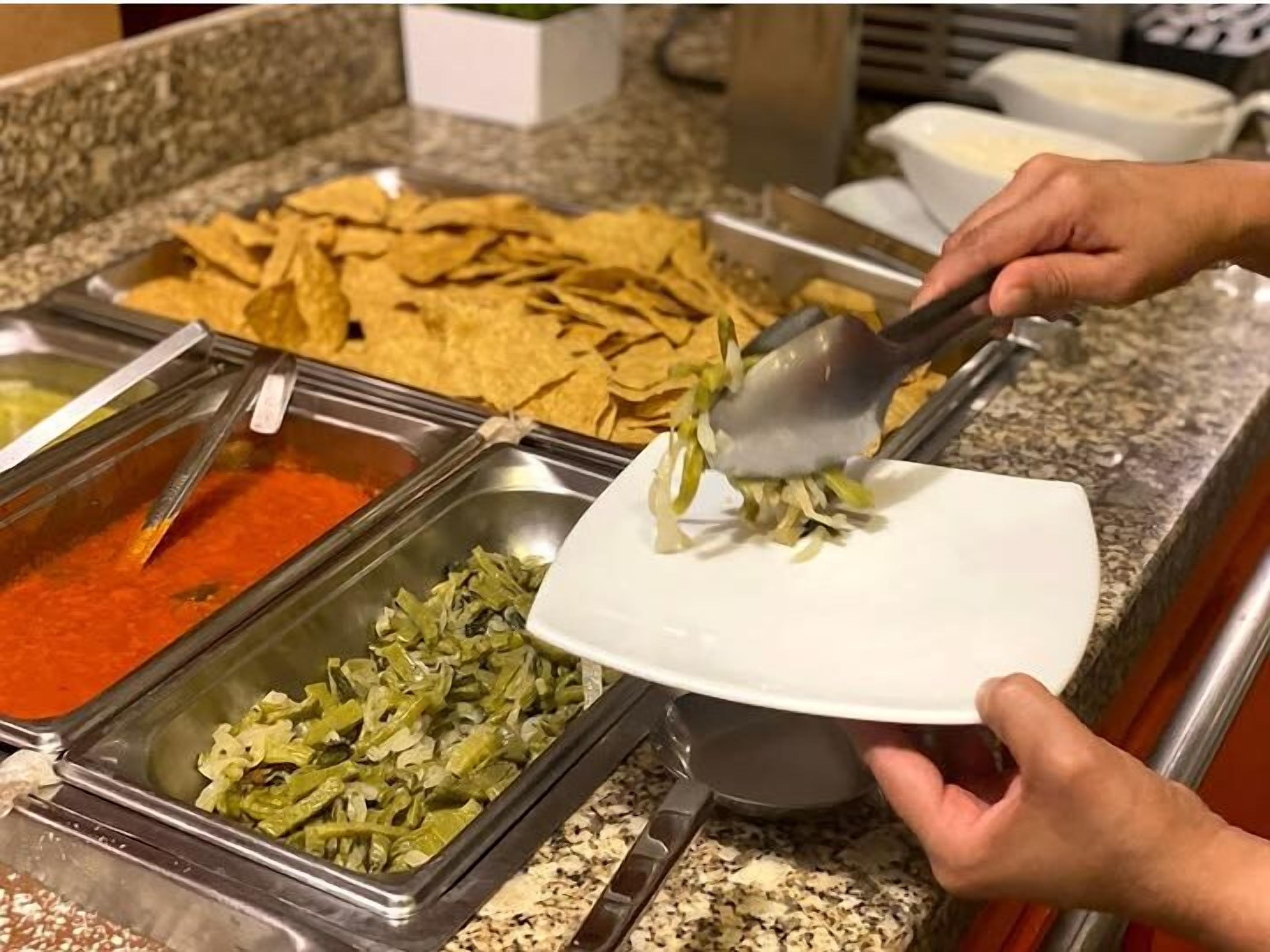 A buffet setup with various food items including nachos, a red sauce, and a green vegetable dish.