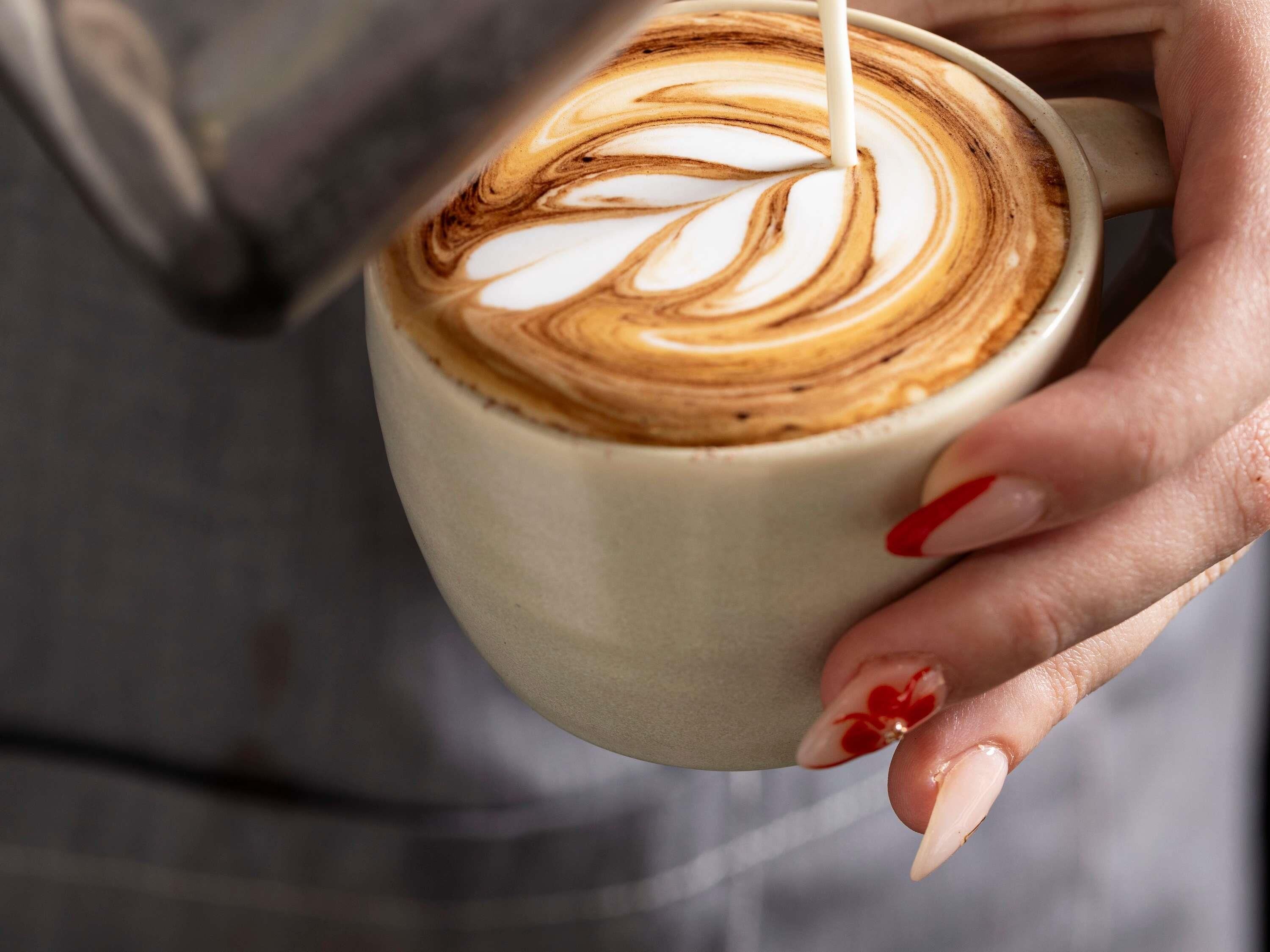 Een close-up van een hand die een koffiekop vasthoudt met latte-kunst.