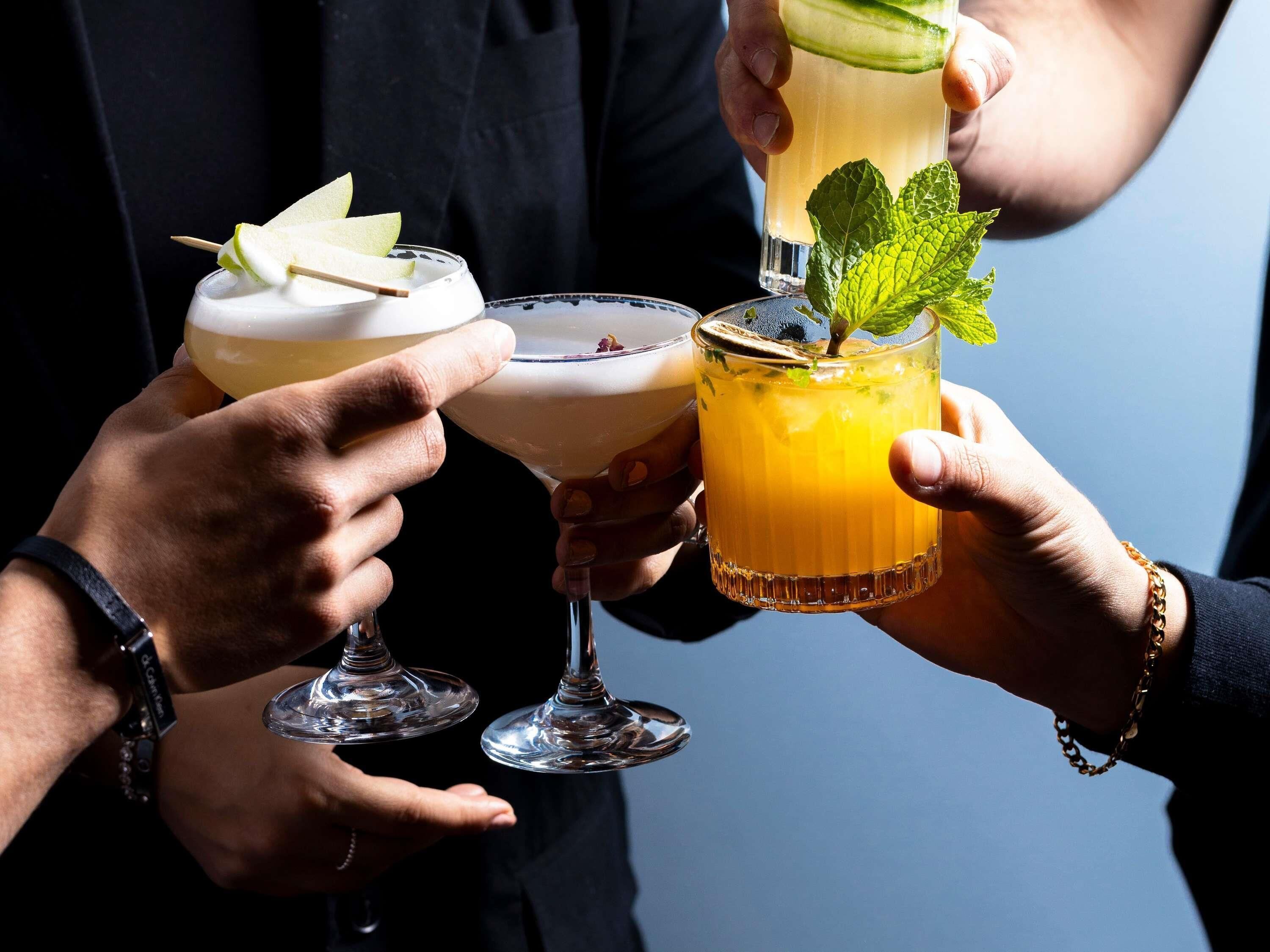 Three people holding drinks with garnishes.