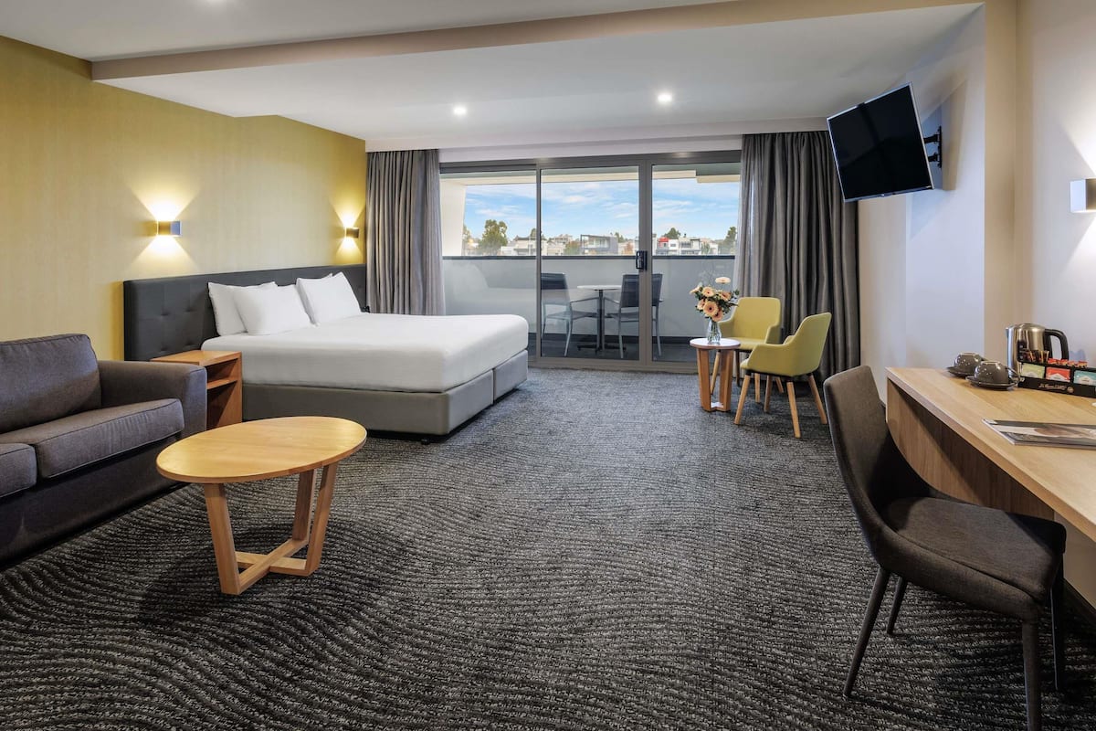 A hotel room with a bed, a sofa, a desk, a chair, a small table, and a TV.