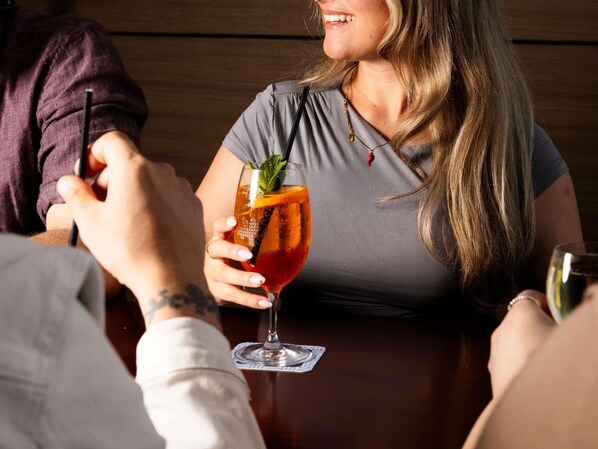 A person holding a cocktail glass with a straw, sitting at a wooden table. - Mercure Melbourne Caroline Springs (Caroline Springs)