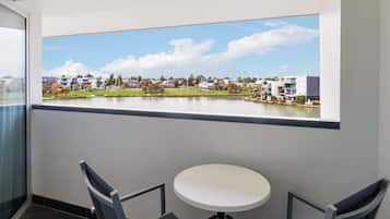 A balcony with a view of a lake and buildings, a round table, and two chairs.