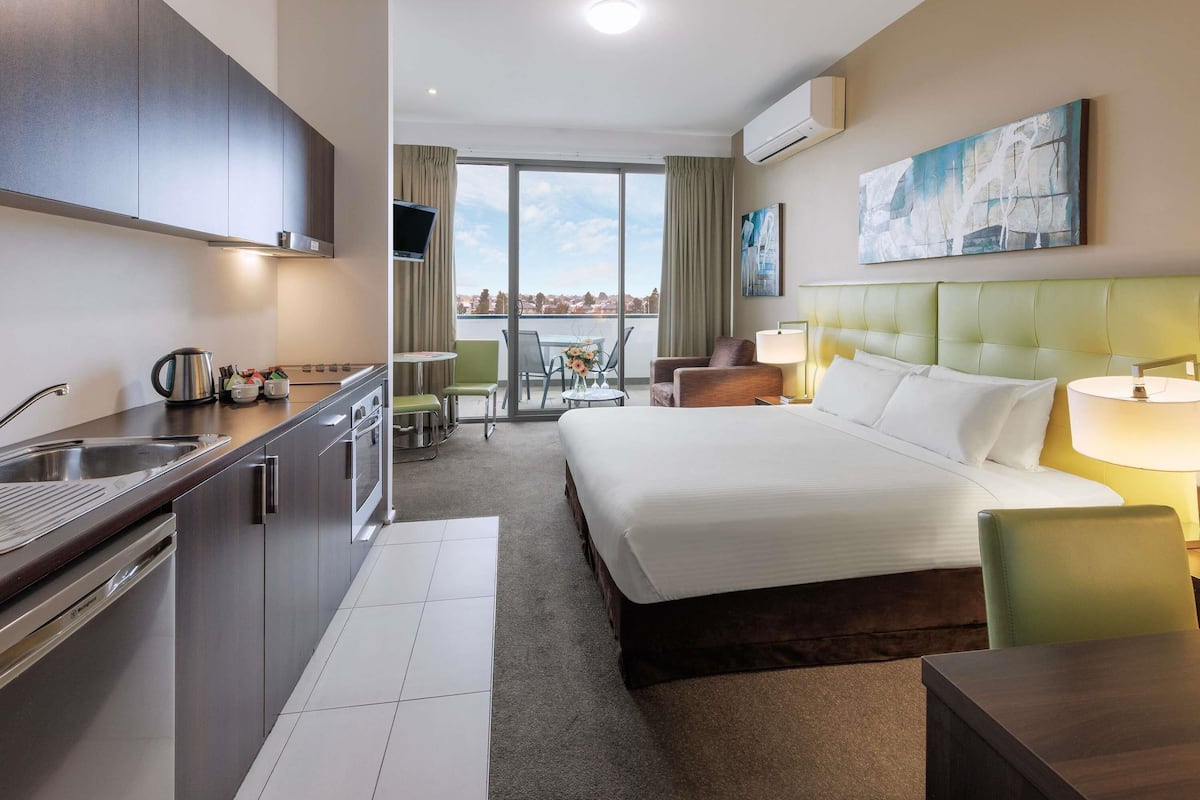 A hotel room with a bed, a desk, a chair, a small table, a sink, and a window with a view.