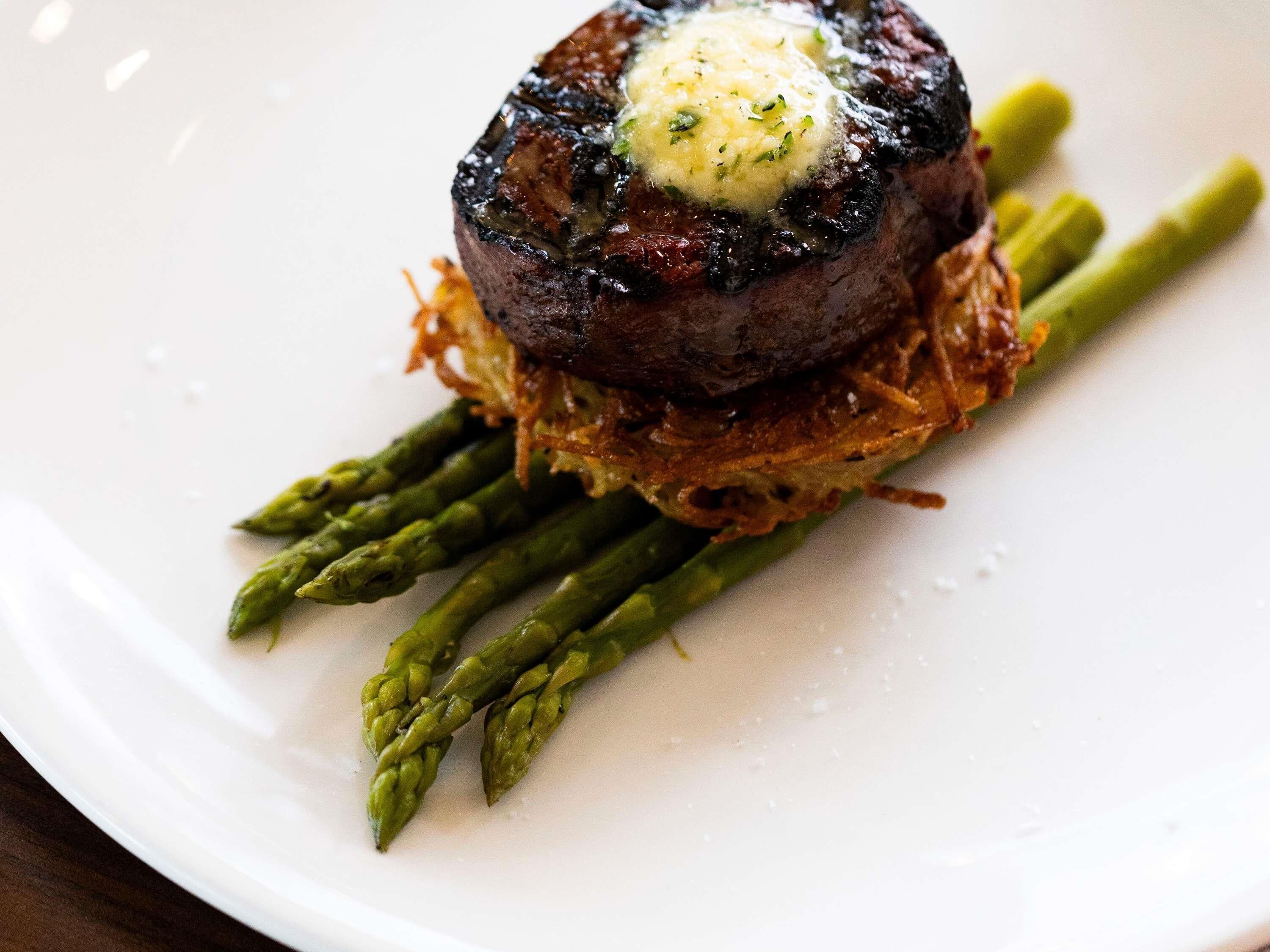 A steak with a pat of butter on top, served with asparagus and a crispy base.