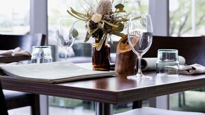 Una mesa de comedor con un menú, un vaso de agua, una copa de vino y un jarrón con flores.