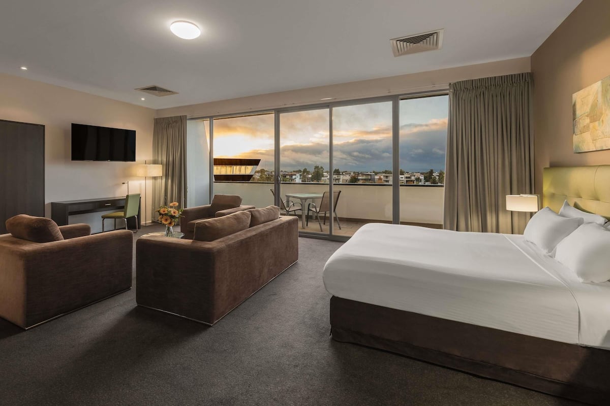 A hotel room with a bed, a sofa, a desk, a TV, and a balcony with a view.