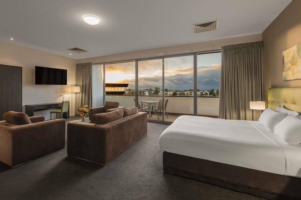Habitación de hotel con cama, dos sofás, un escritorio y un ventanal con vistas.