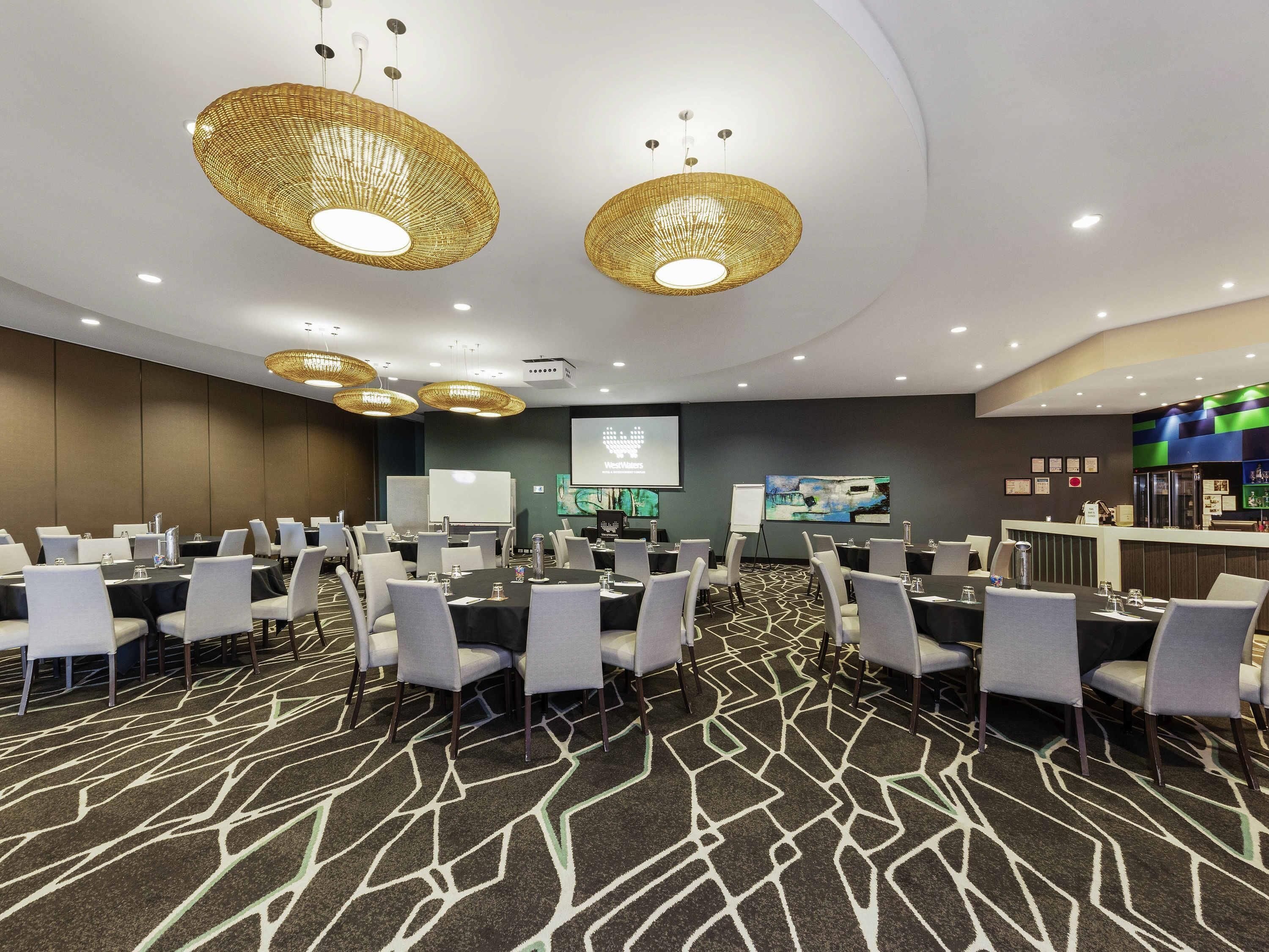 A conference room with round tables, chairs, a projection screen, and a bar area.