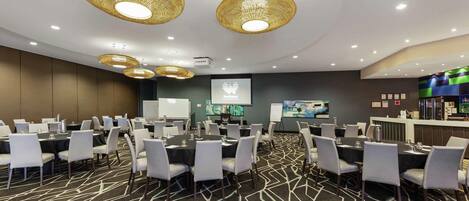 A conference room with round tables, chairs, a projection screen, and a bar area.