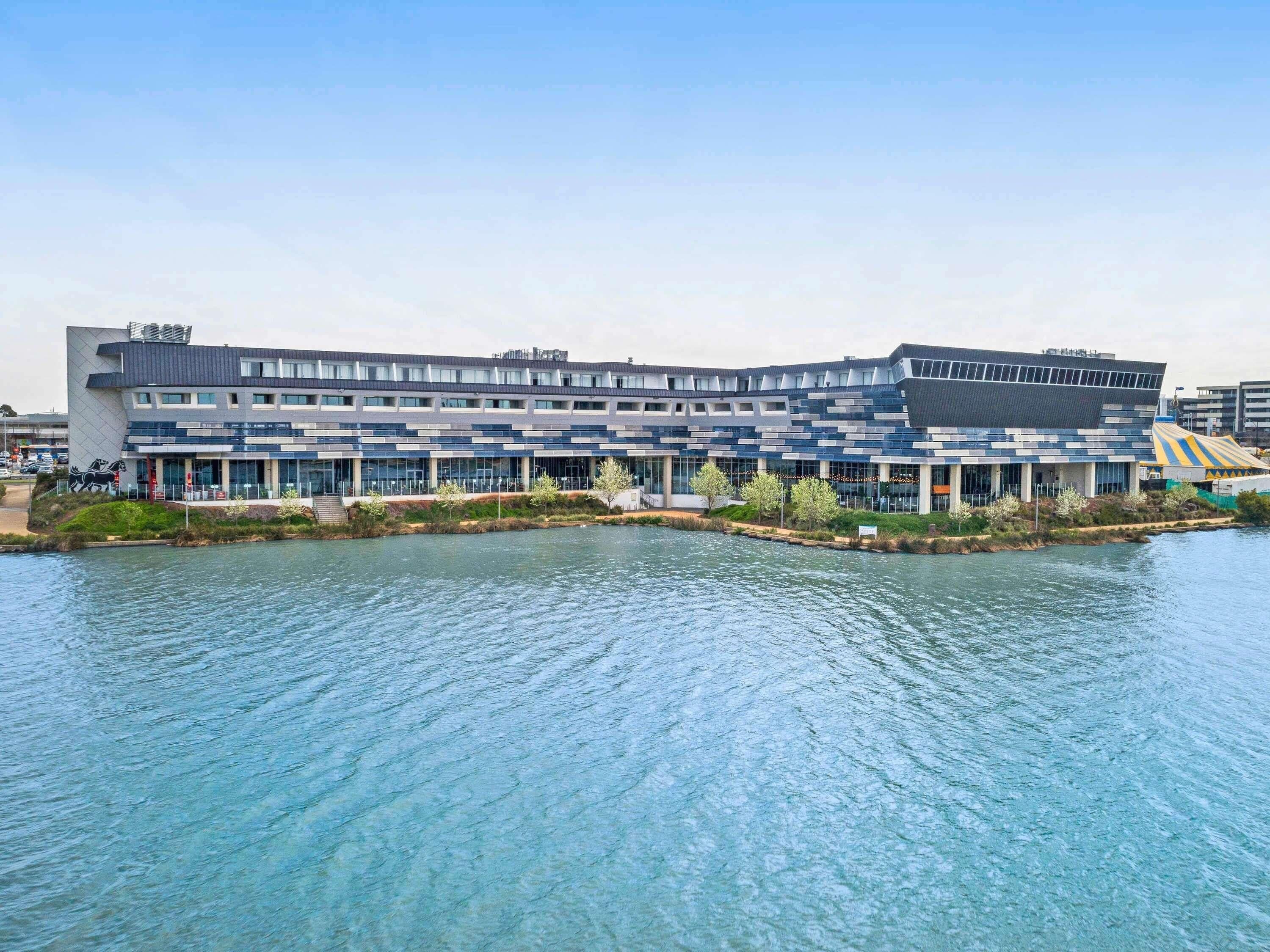 A modern building with a flat roof, large windows, and a water body in front.