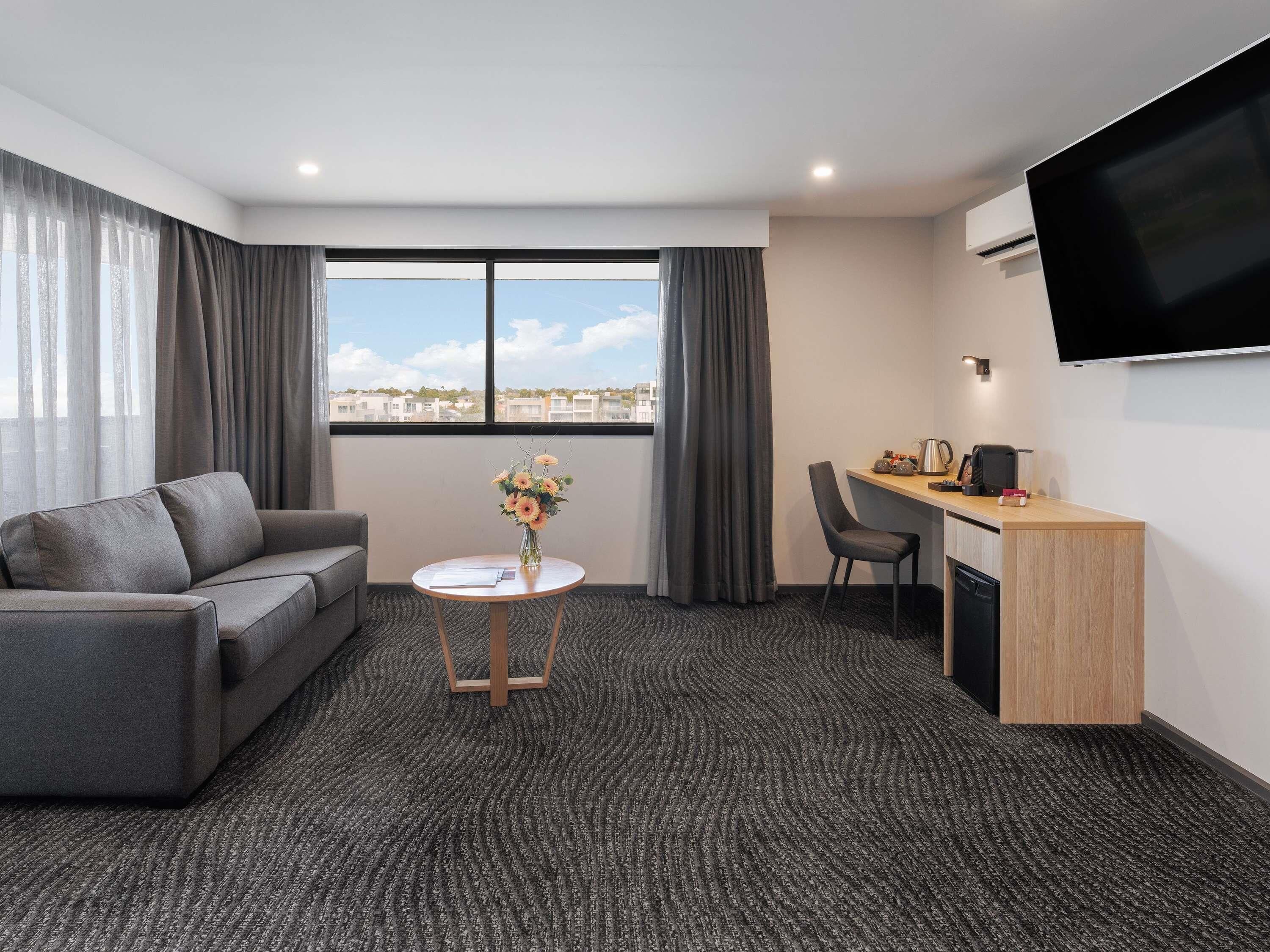 Een hotelkamer met een bank, een klein rond tafeltje met een vaas, een bureau met een stoel en een aan de muur bevestigde televisie.