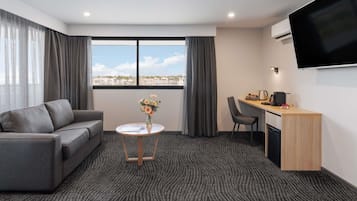 Een hotelkamer met een bank, een klein rond tafeltje met een vaas, een bureau met een stoel en een aan de muur bevestigde televisie.