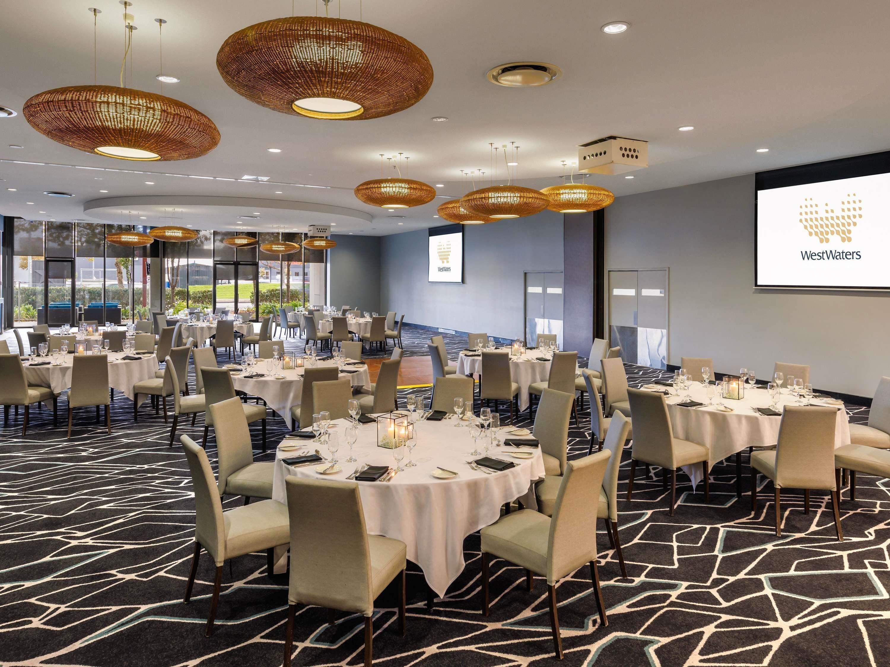 Een congreszaal met ronde tafels, stoelen en een groot scherm waarop het WestWaters logo wordt getoond.