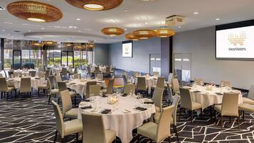 Een congreszaal met ronde tafels, stoelen en een groot scherm waarop het WestWaters logo wordt getoond.