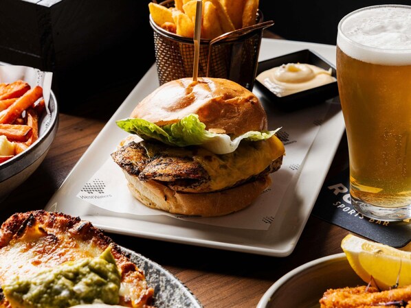 Una hamburguesa acompañada de papas fritas, una cerveza en vaso y un gajo de limón sobre una mesa.