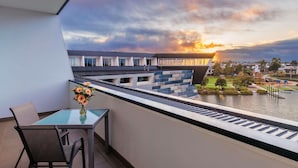 Un balcón con mesa y sillas, con vista a un cuerpo de agua y un moderno complejo de edificios.