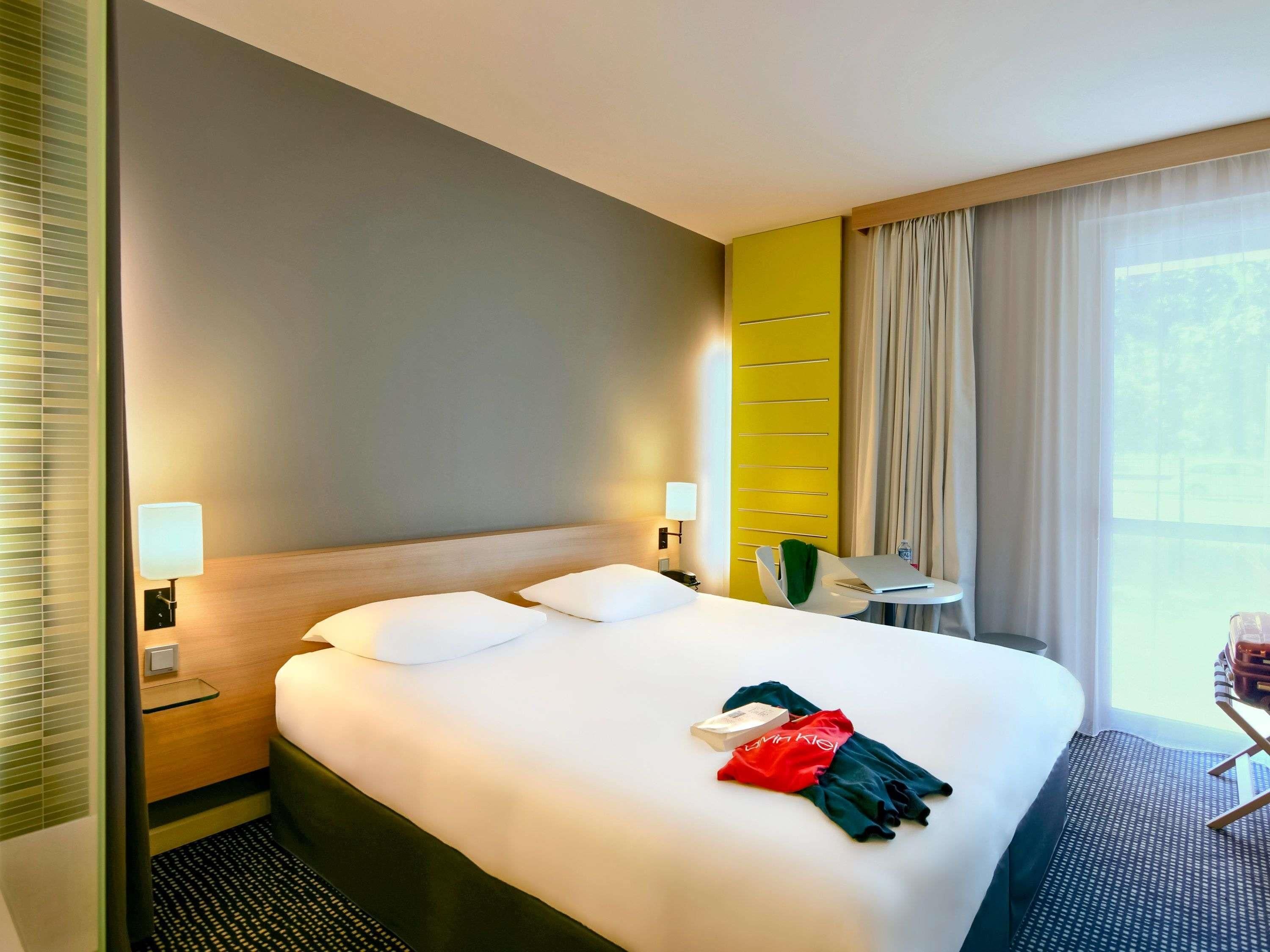 Een hotelkamer met een bed, nachtlampjes, een klein tafeltje en een stoel.