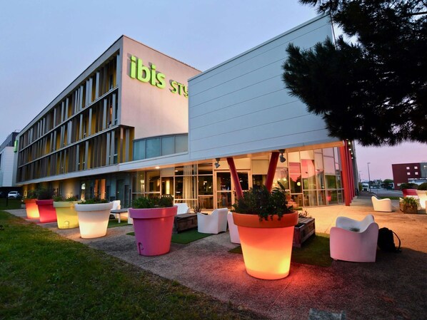 A modern hotel with a prominent 'ibis' sign, large potted plants, and a well-lit entrance. - ibis Styles Nantes Rezé Aéroport (Reze)