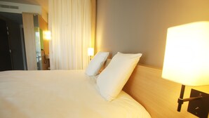 Une chambre d’hôtel avec un grand lit, deux oreillers, une lampe de chevet et une porte donnant sur une salle de bain.