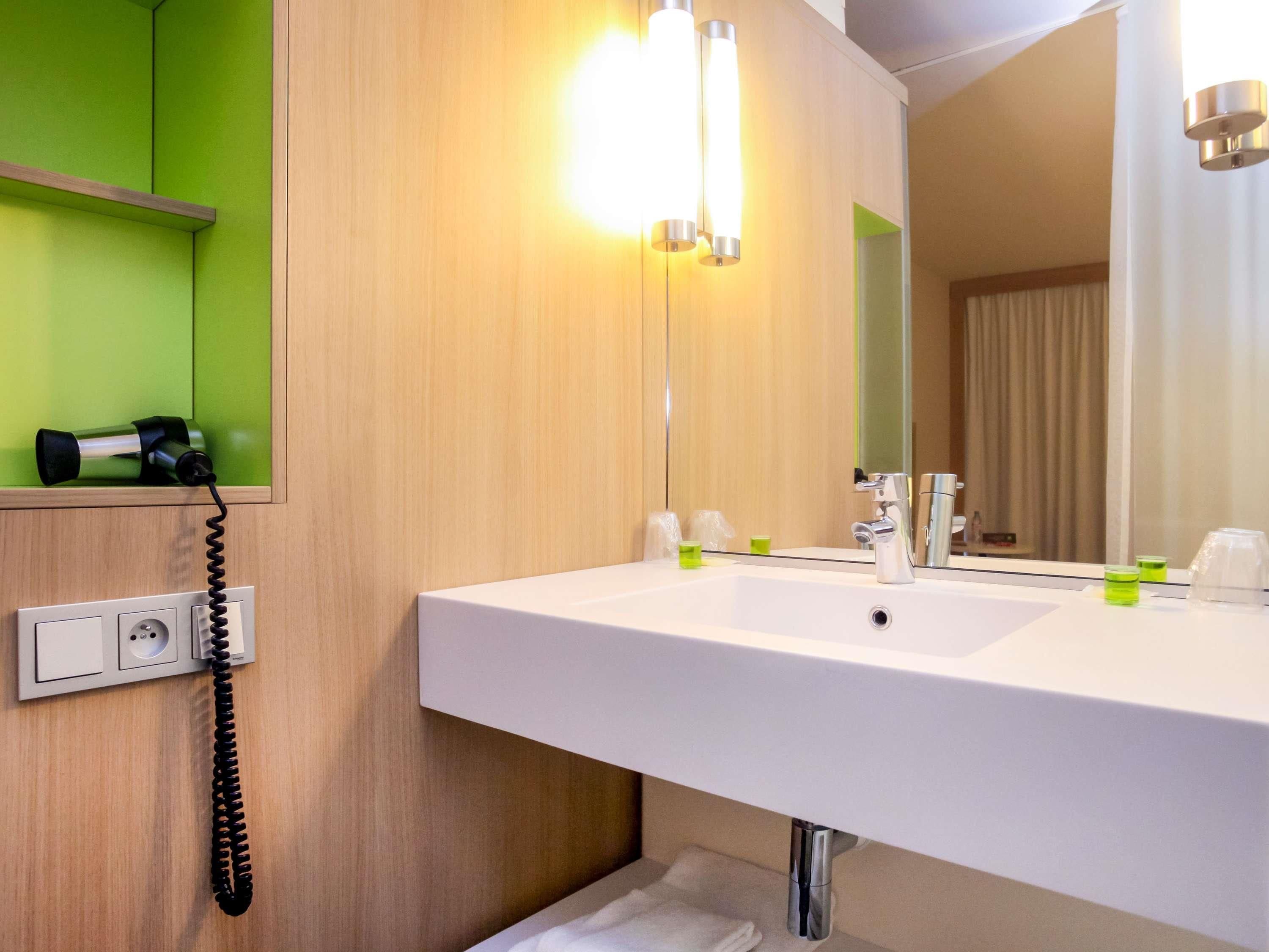 Ein Badezimmer mit weißem Waschbecken, einem Spiegel, einem Telefon und einer grünen Wand.