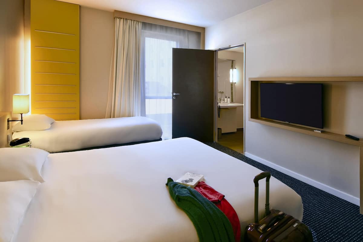Habitación de hotel con dos camas, televisión, baño y vistas a la ciudad.