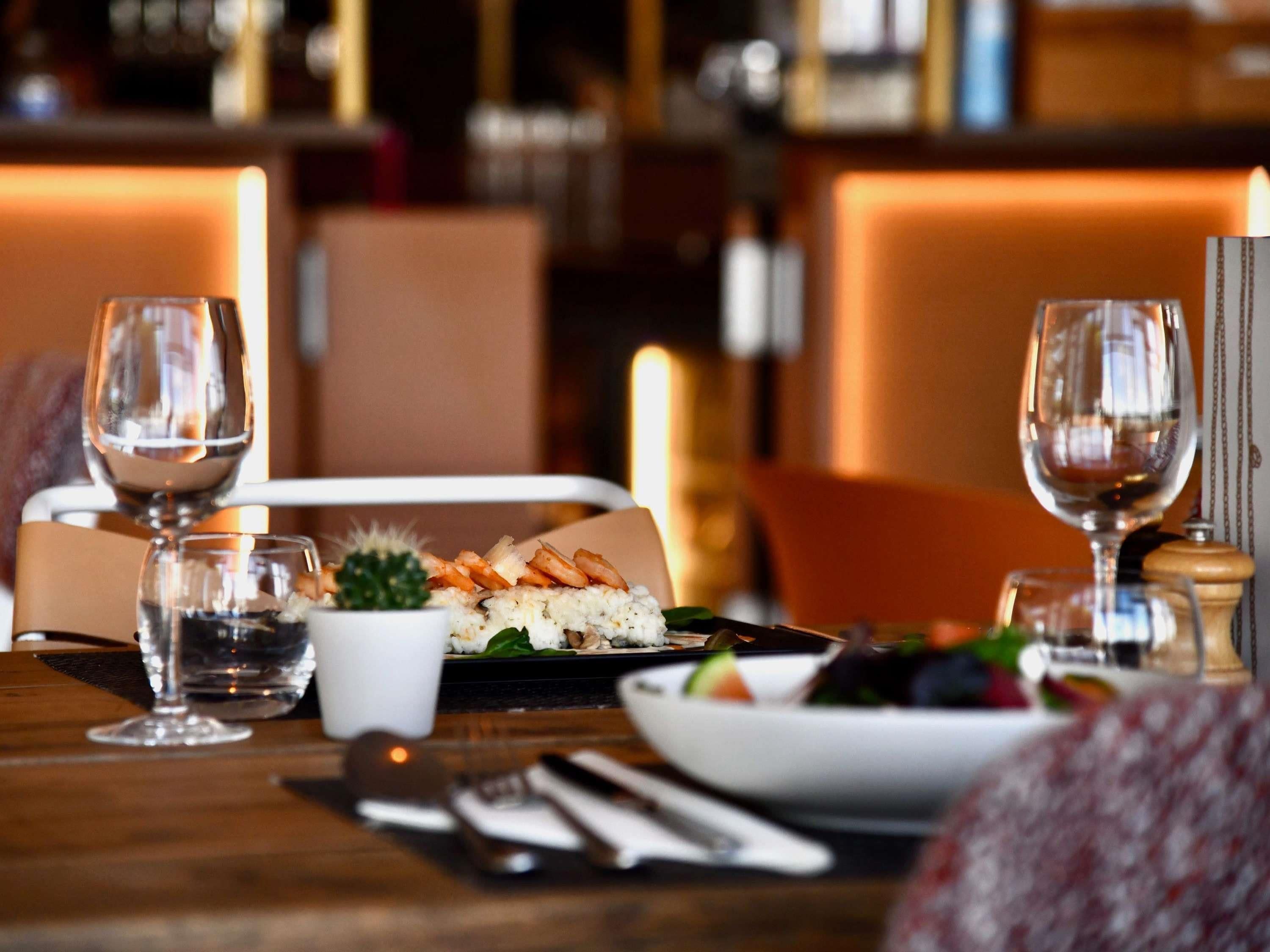 A dining table set with a plate of sushi, a bowl of salad, and two wine glasses.