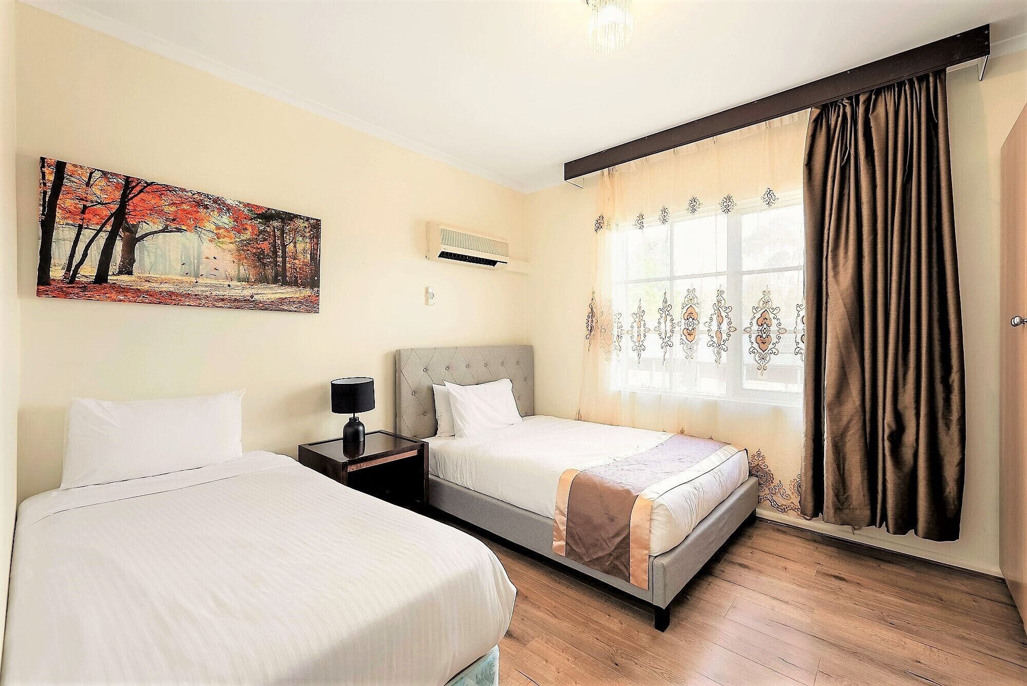 Une chambre d’hôtel avec deux lits, un tableau au mur, un appareil de climatisation et une fenêtre avec des rideaux.
