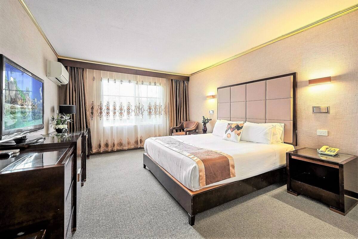 A hotel room with a large bed, a desk with a TV, a telephone, and a nightstand.