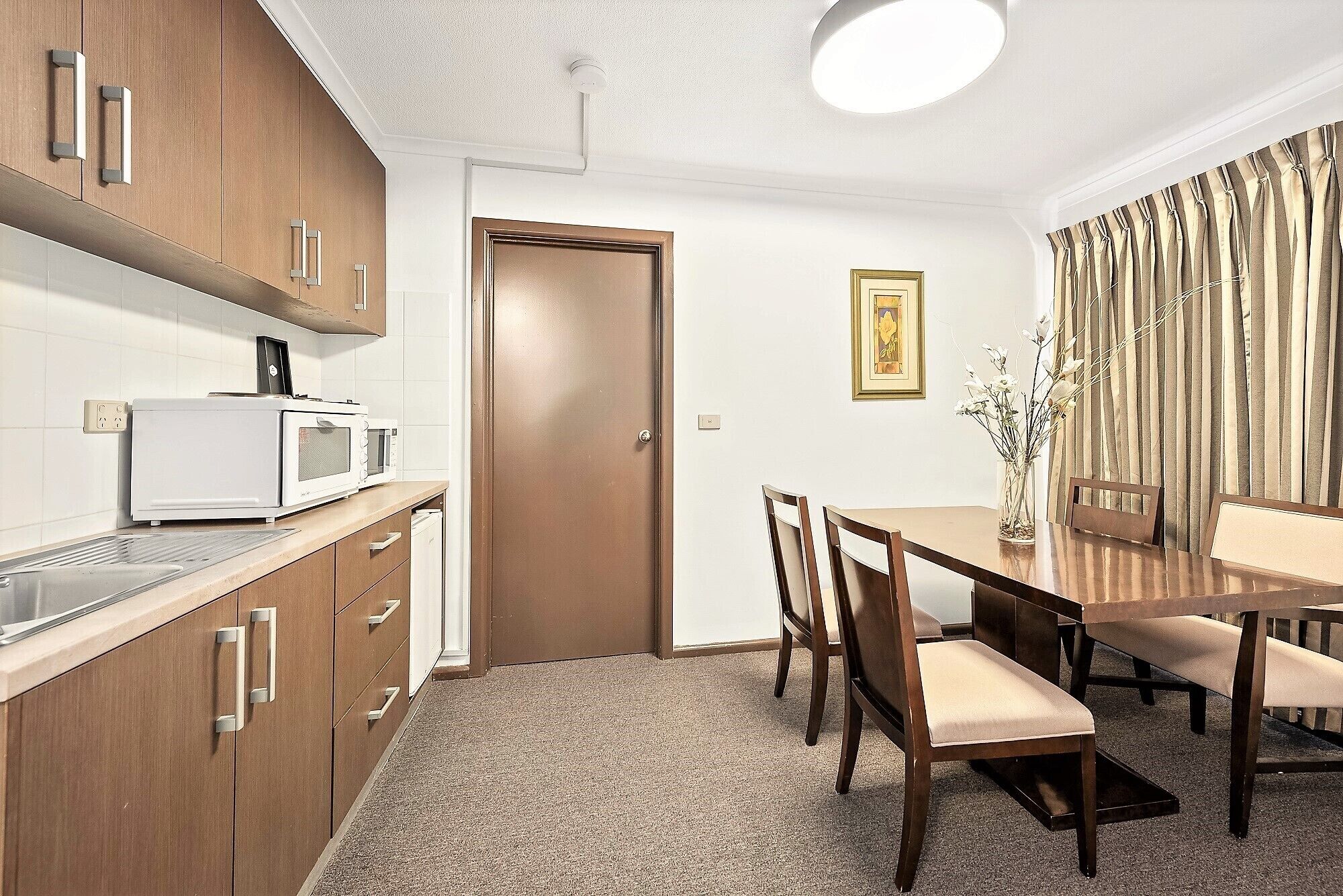 A compact kitchen with a microwave, toaster, and cabinets. There is a dining area with a table and chairs, and a door leading to another room.