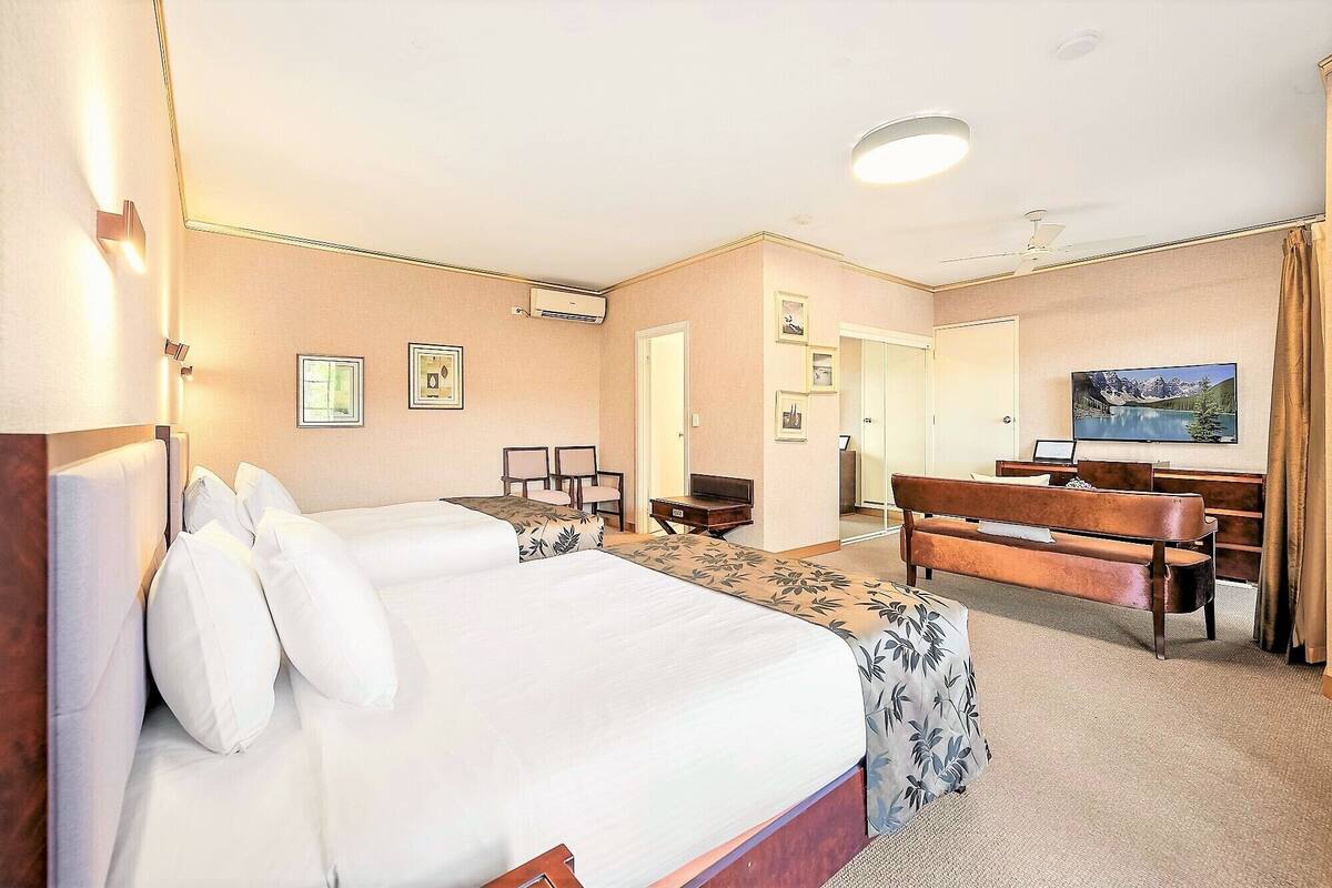 A hotel room with a bed, a desk, a chair, a TV, and a painting on the wall.