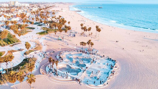 Vue aérienne d’une plage avec une grande zone de piscine, des palmiers et, au loin, le paysage urbain de la côte.