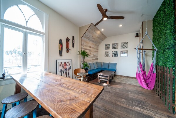 A spacious living area with a wooden dining table, blue bar stools, a blue sofa, and a hammock.