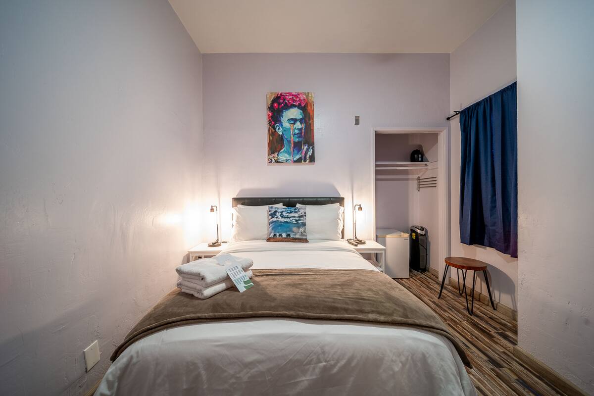 Une chambre d’hôtel avec un lit, des lampes de chevet, un tableau au mur, une petite table et une armoire.
