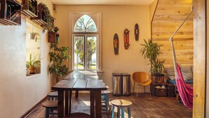 Un espace repas avec une table et des tabourets en bois, un hamac et des plantes en pot.