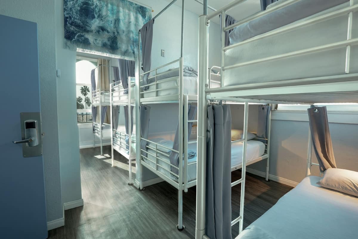 Une chambre avec des lits superposés, donnant sur des palmiers, une porte avec une serrure et une fenêtre avec des rideaux.