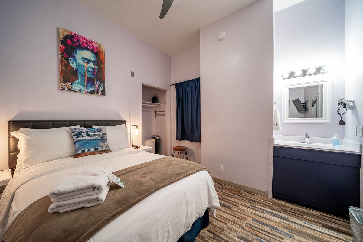 Une chambre d’hôtel avec un lit, une table de chevet, une commode, un miroir avec éclairage, un lavabo et une serviette sur le lit.