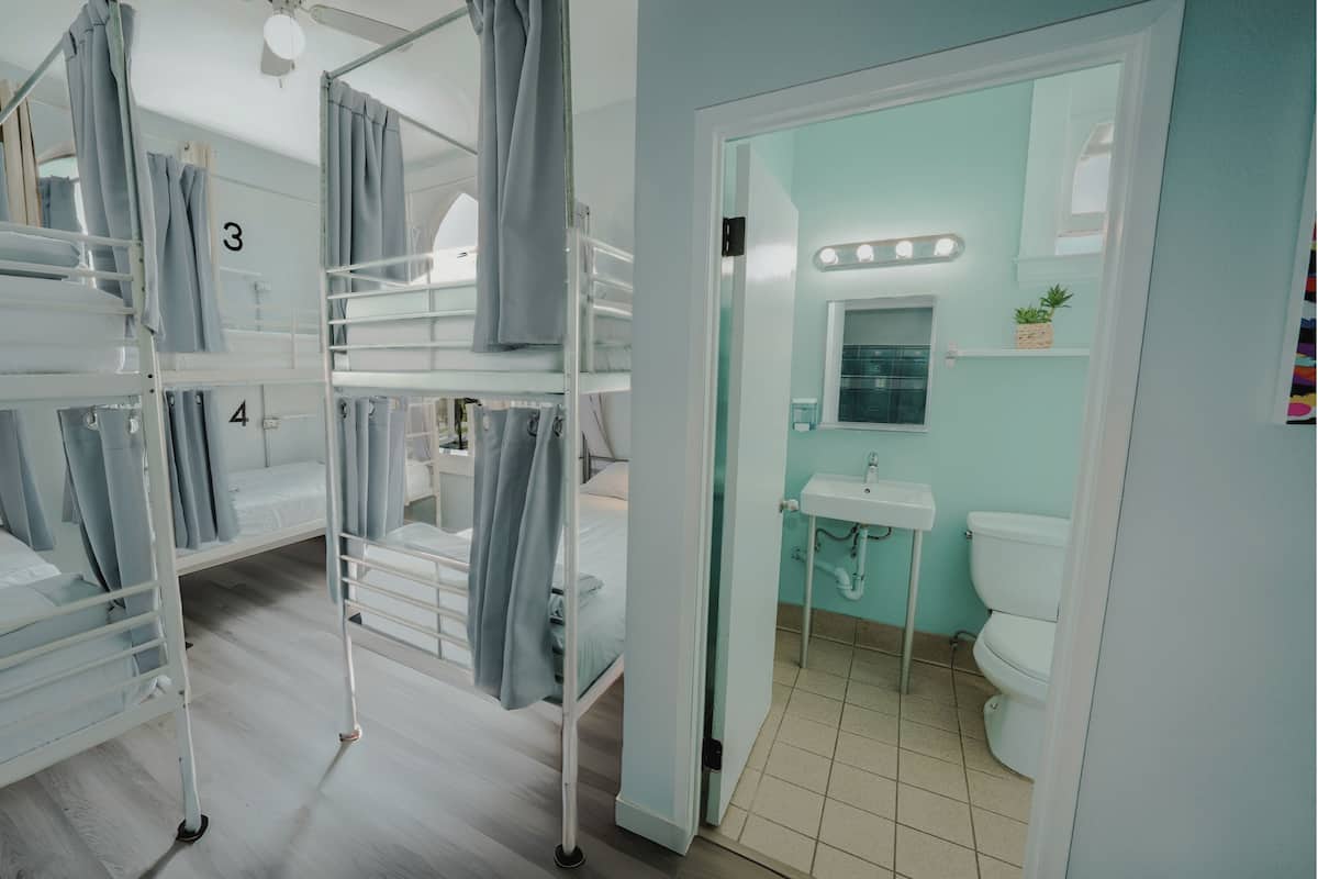 Une chambre avec deux lits superposés, numérotés 3 et 4, une salle de bain avec un lavabo et des toilettes, et un miroir avec éclairage.