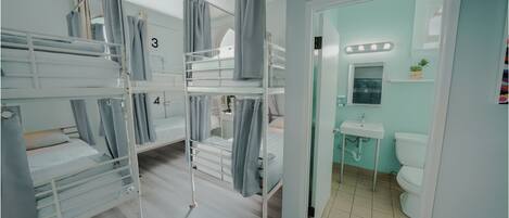 A room with bunk beds numbered 3 and 4, a bathroom with a sink and toilet, and a mirror with lights.