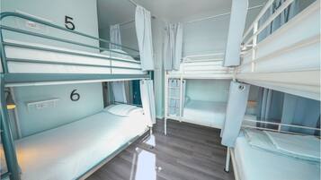 Une chambre avec des lits superposés numérotés 5 et 6, un espace douche et une petite étagère avec une lampe.