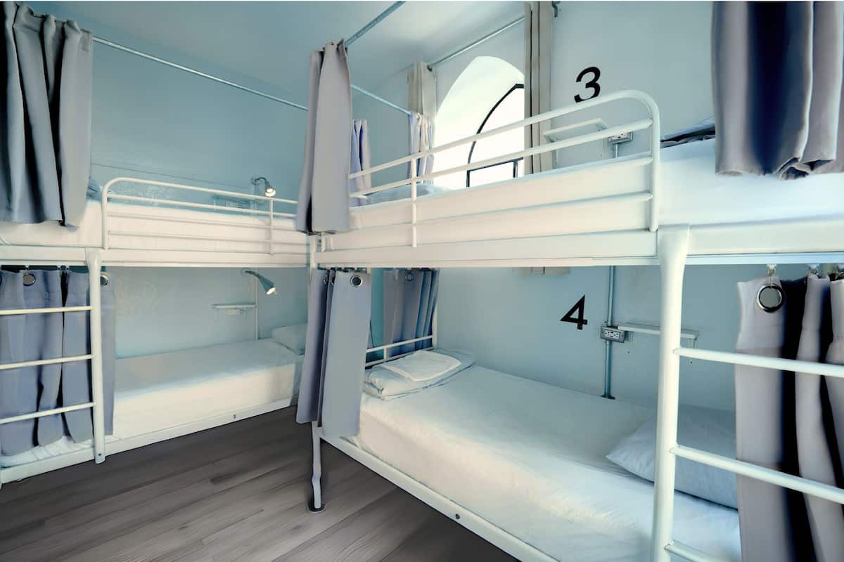 Une chambre avec deux lits superposés, les lits numérotés 3 et 4, des rideaux et une fenêtre.