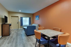 A hotel room with a dining area, a television, a sofa, and a painting on the wall. - Captains Quarters Inn Port Aransas TX (Port Aransas)