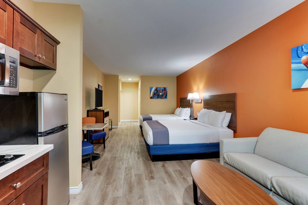 A hotel room with a kitchenette, a bed, a sofa, and a dining area.
