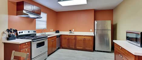 A kitchen with wooden cabinets, a stainless steel refrigerator, a microwave, and a stove.