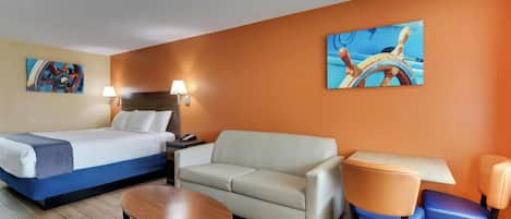 A hotel room with a bed, a sofa, a table, and two chairs. There are two wall-mounted lamps and two paintings.